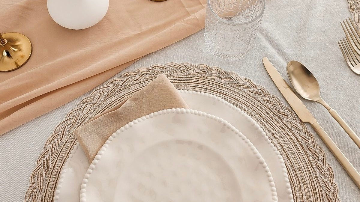 Elegant table setting with neutral placemats, gold cutlery, glass cup and beige napkin