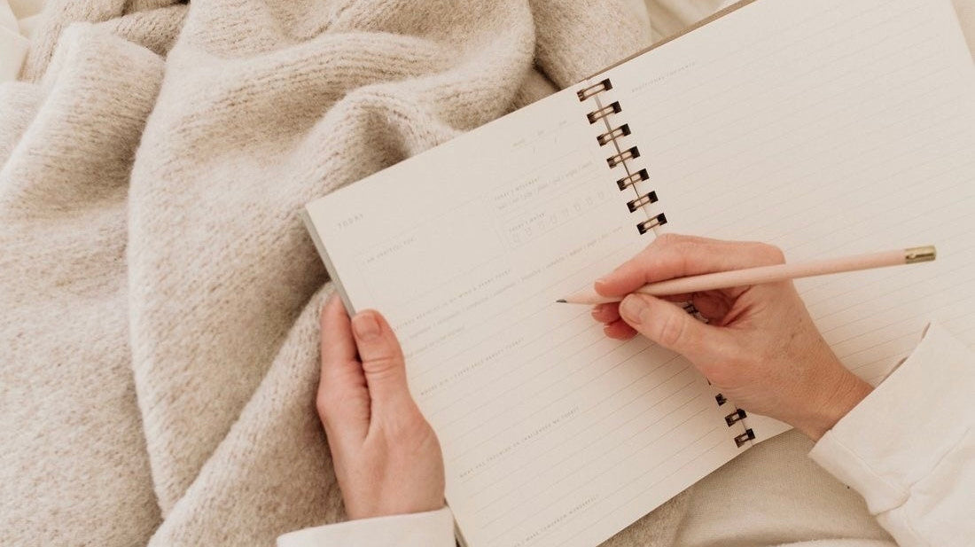 Woman journaling on cozy beige blanket, promoting thoughtful modest clothing lifestyle