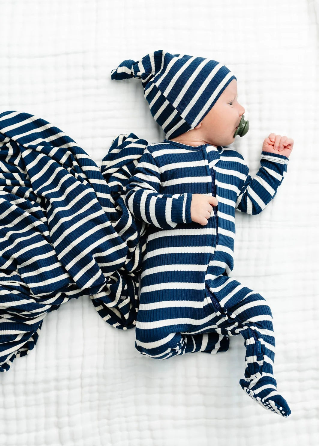 Baby in blue and white striped outfit and hat lying on a white blanket