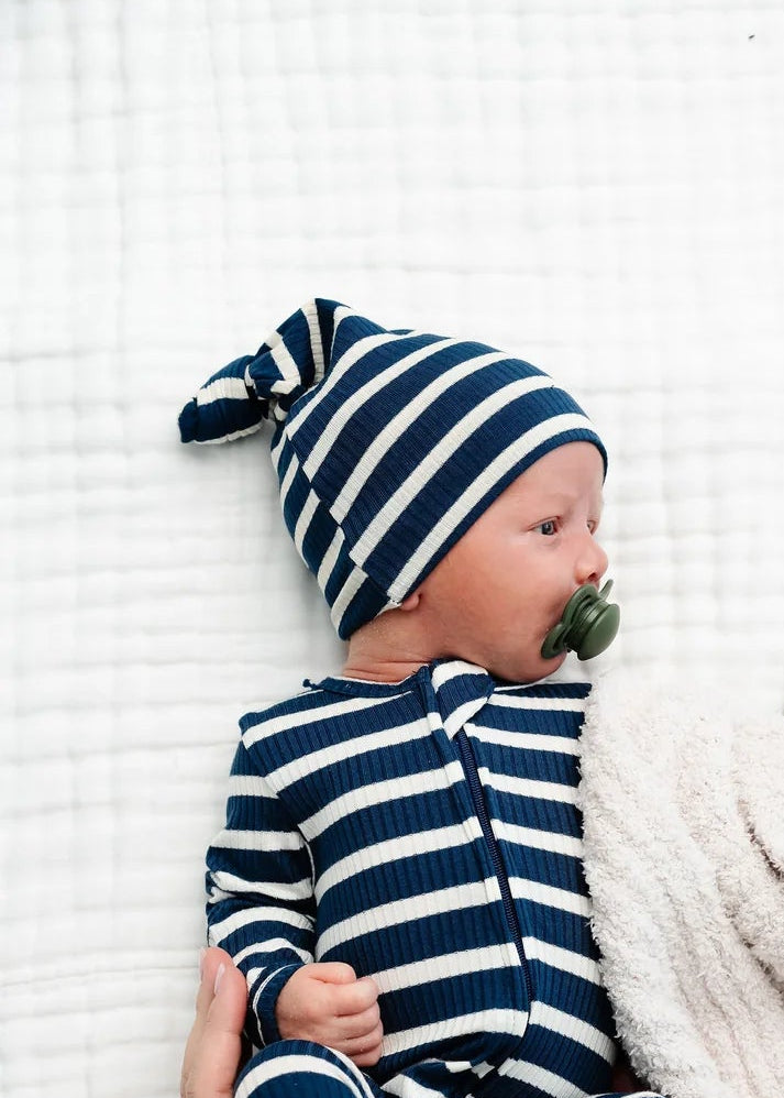 Baby in a striped outfit and hat being held on a white blanket