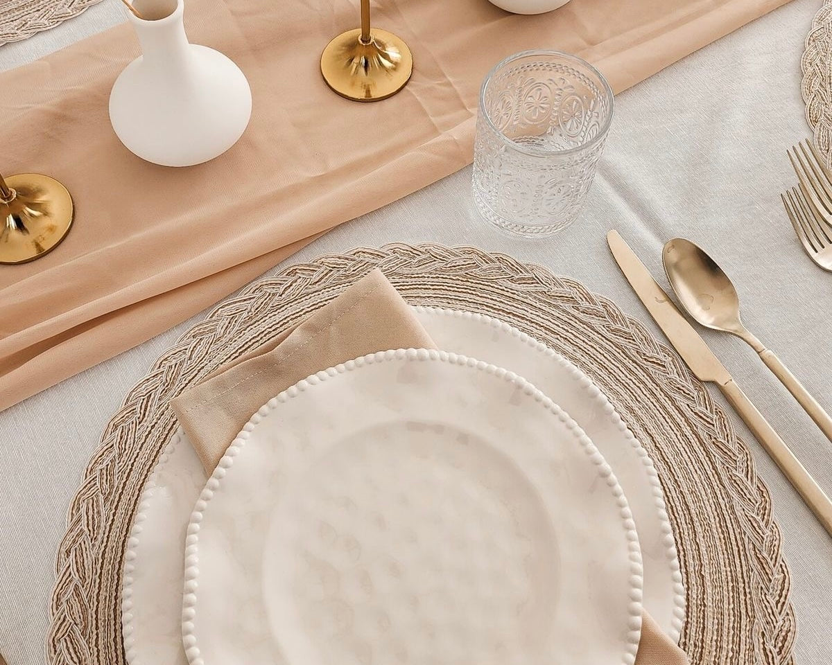 Elegant table setting with neutral placemats, gold cutlery, glass cup and beige napkin