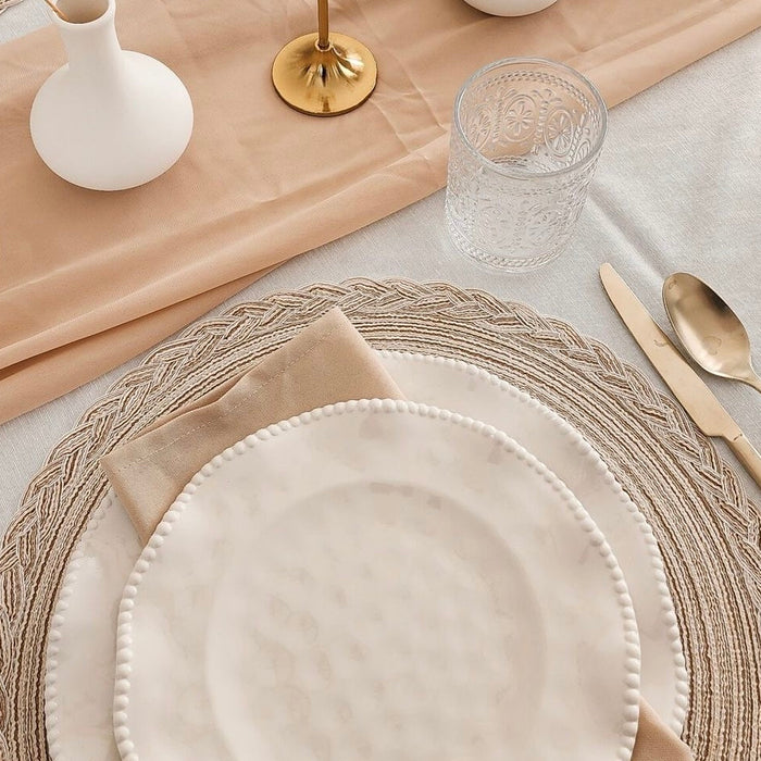 Elegant table setting with neutral placemats, gold cutlery, glass cup and beige napkin