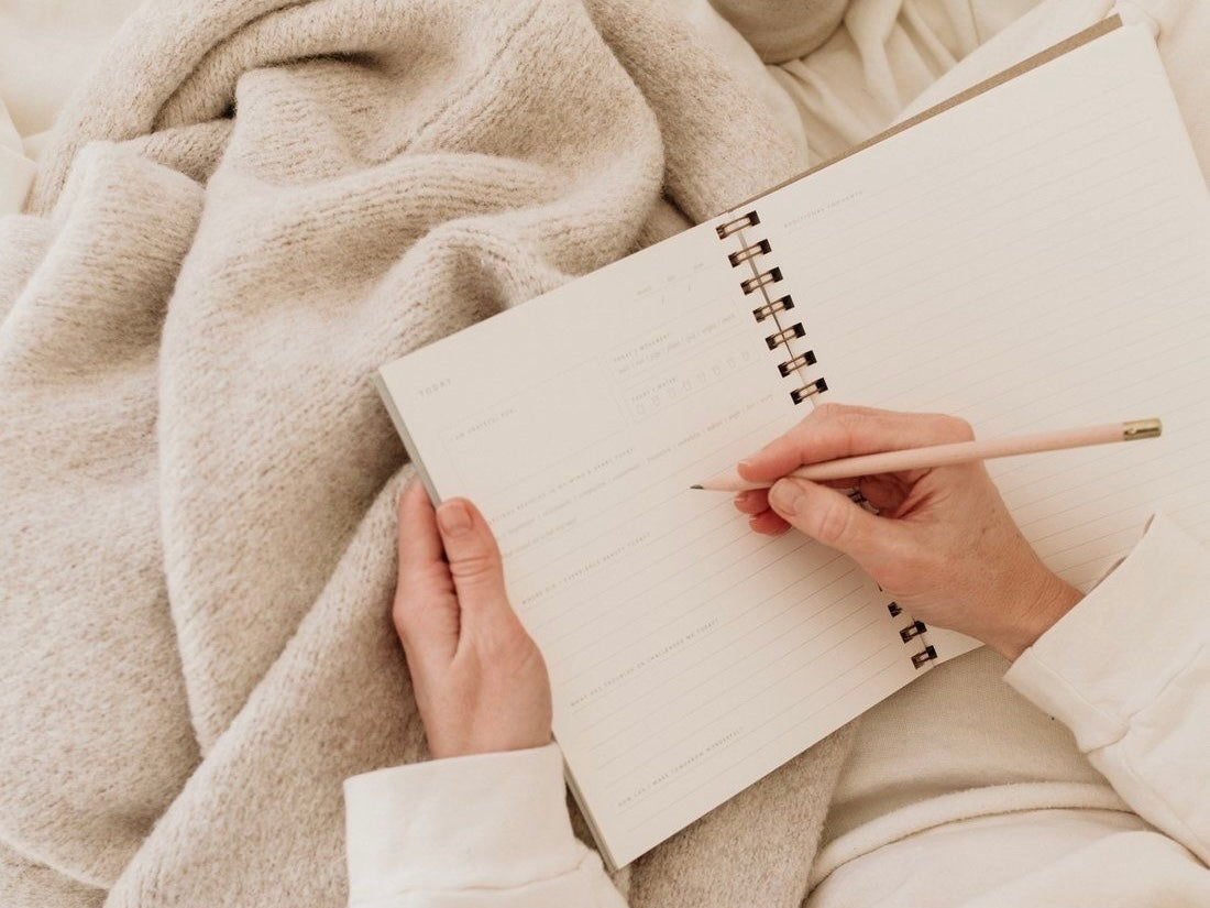 Woman journaling on cozy beige blanket, promoting thoughtful modest clothing lifestyle