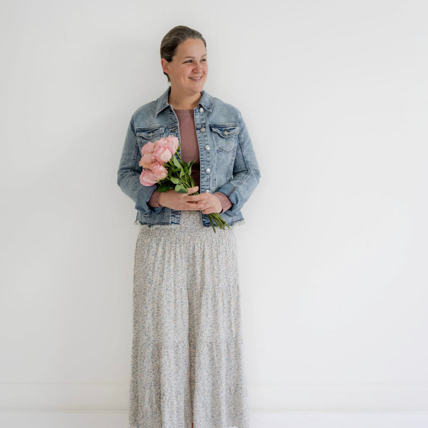 Woman in modest floral maxi skirt and denim jacket holding pink flowers, Salt and Honey boutique