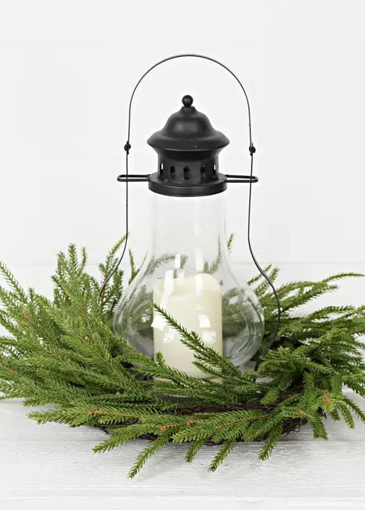 Decorative lantern with a candle surrounded by greenery on a white background