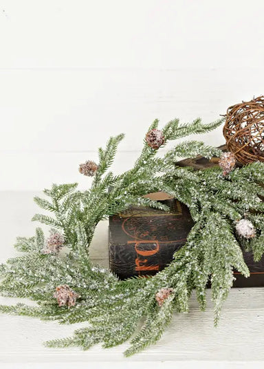 Decorative wreath with pine branches and a decorative ball on a wooden box against a white background