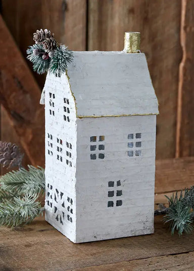 Decorative house-shaped lantern with pinecones and greenery on a wooden surface