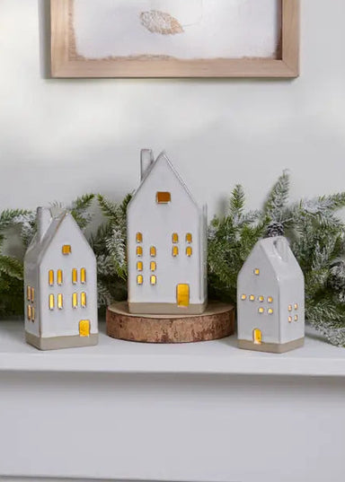 Decorative house-shaped candles on a mantelpiece with candles and greenery.
