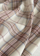 A close-up of draped fabric with a plaid pattern in cream, beige, brown, and light blue.