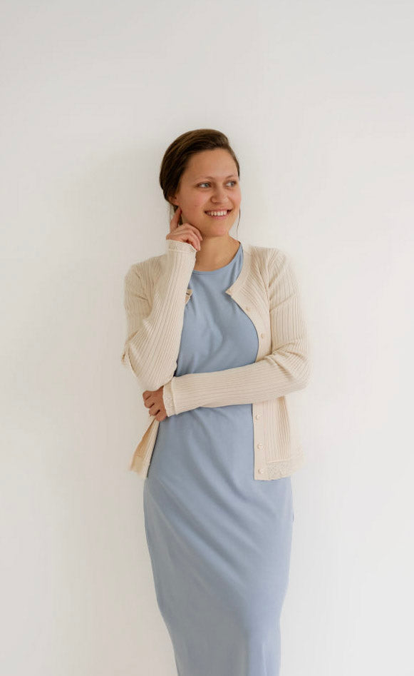 Woman wearing a light blue dress with a beige cardigan against a white background