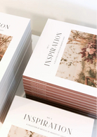 Stacks of printed art books or magazines titled "INSPIRATION" with a floral cover photo, arranged on a light neutral surface.