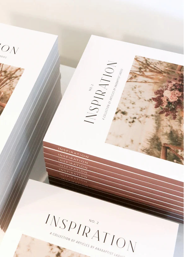 Stacks of printed art books or magazines titled "INSPIRATION" with a floral cover photo, arranged on a light neutral surface.