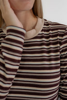 Close-up of a person wearing a ribbed long-sleeve top with horizontal stripes in dark brown, beige, and white, featuring a solid beige crew neck.