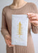 A person holding a white paper napkin with a gold tree print and the text 'Glory to God' on it.