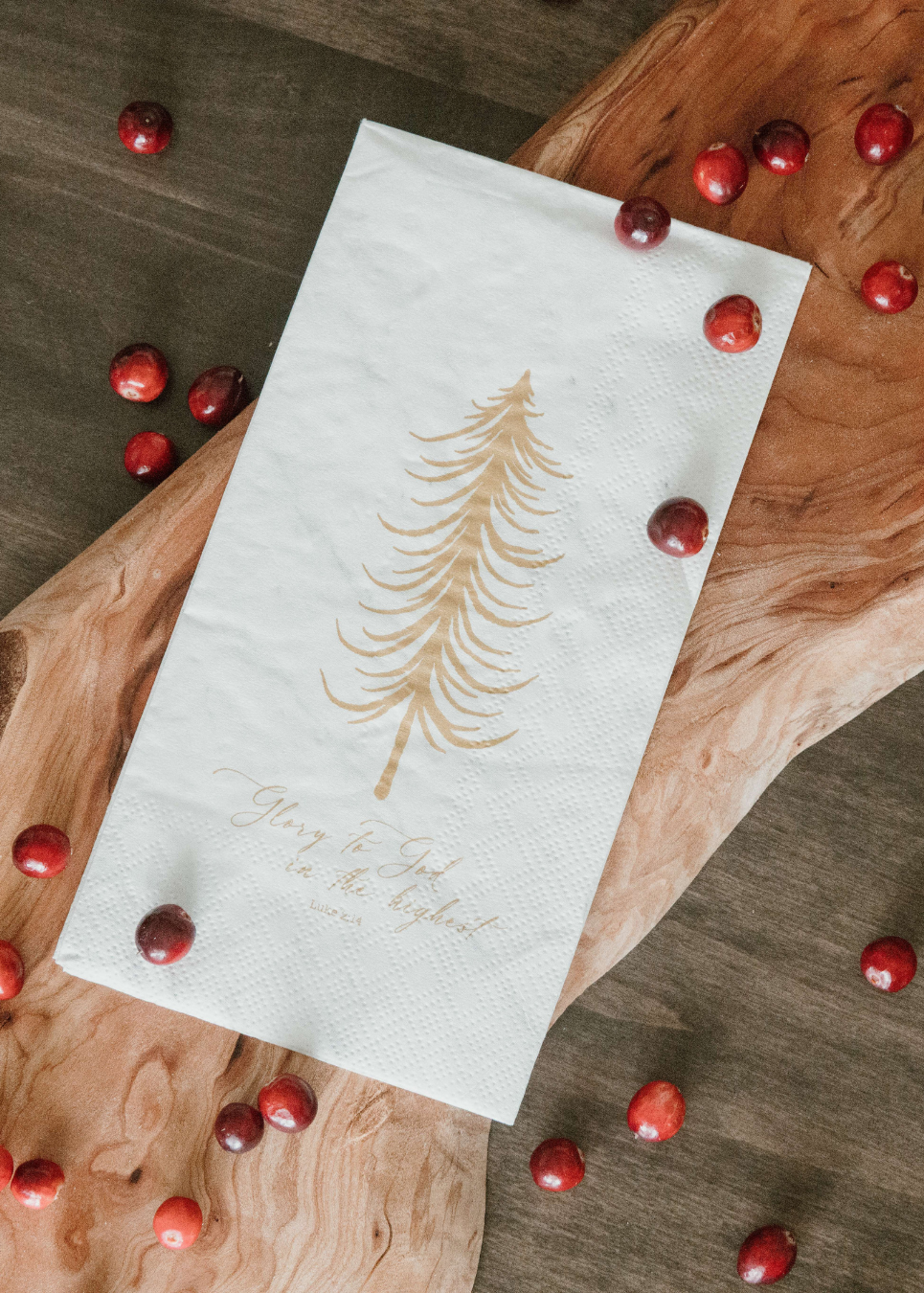 White napkin with gold tree design and text on a wooden surface with red berries
