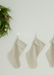 Three striped stockings hanging on a white wall with a green wreath in the corner.