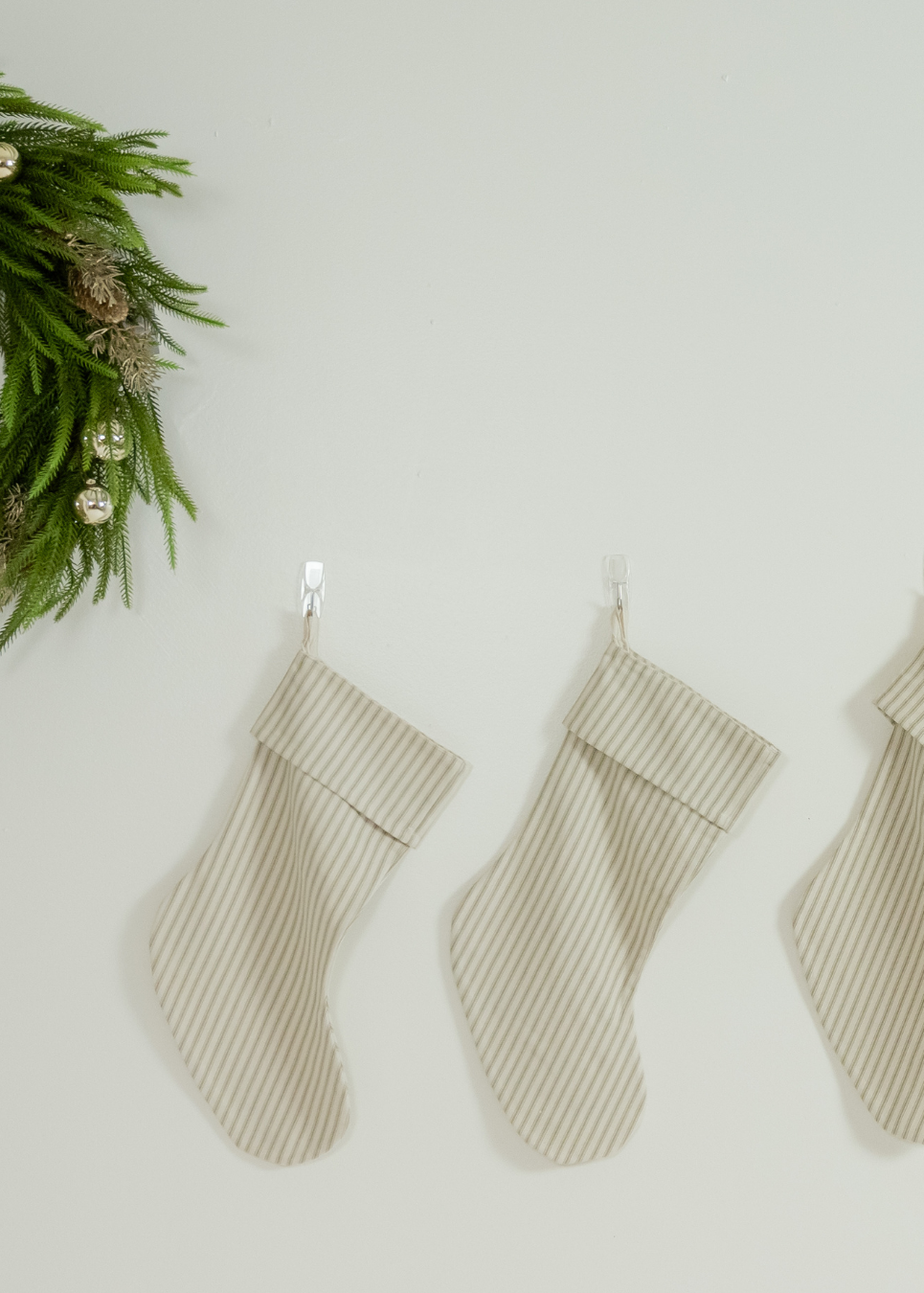 Three striped stockings hanging on a white wall with a green wreath in the corner.