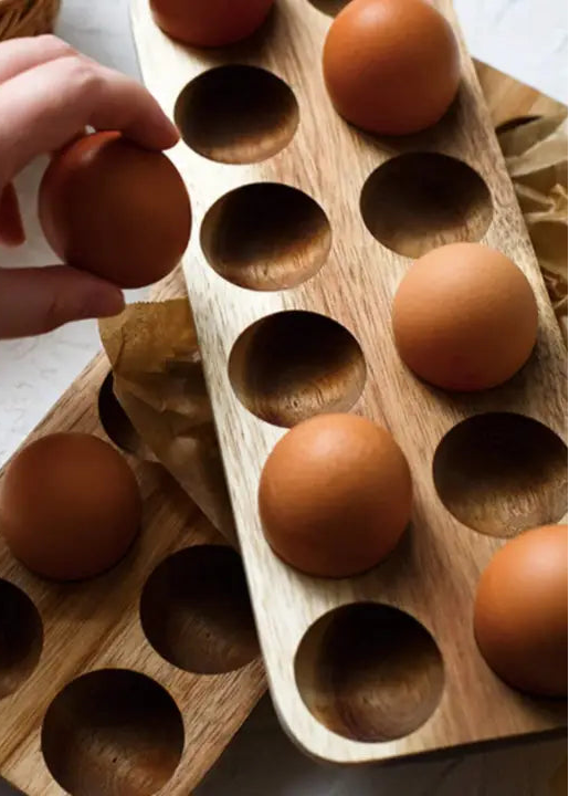 Person placing a brown egg into a wooden egg holder on a light surface.