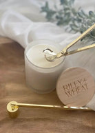 Candle with a wooden lid and gold candle snuffer on a wooden surface.