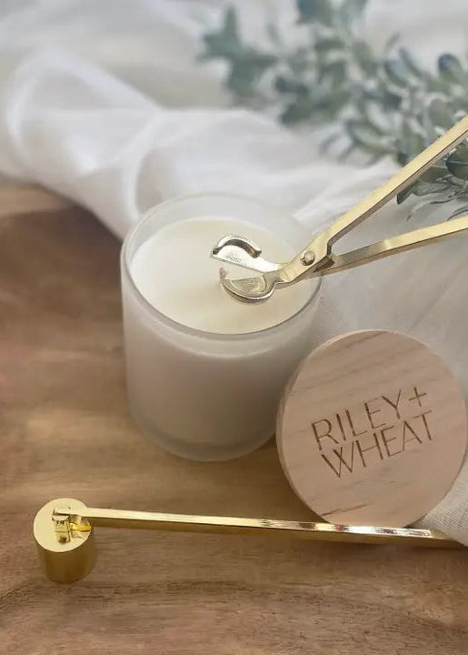 Candle with a wooden lid and gold candle snuffer on a wooden surface.