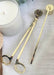 Gold candle snuffers and a white candle with a wooden lid on a textured surface.