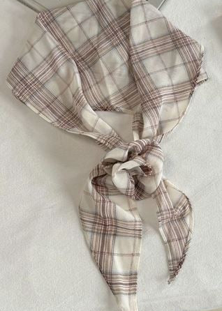 A lightweight square scarf with a beige and brown plaid pattern, tied in a knot and draped on a white fabric surface.