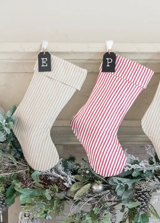 Three Christmas stockings hanging on a mantel with decorative greenery.