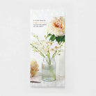 Sympathy card with soft pink peonies and white flowers in a glass vase on a white table.
